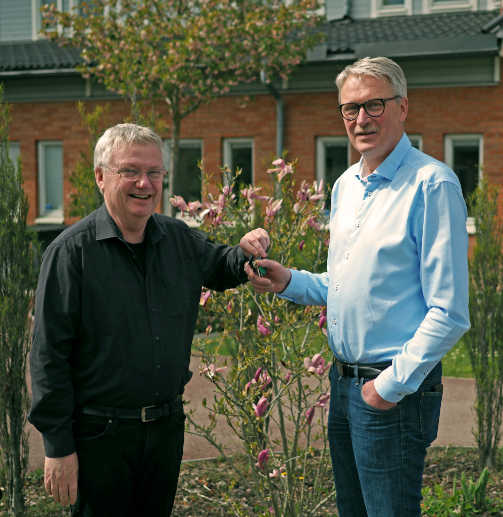 Two men standing in a courtyard, smiling. Magnus, Fodina's retiring CEO, hands over the keys to the office to our new CEO Micke.